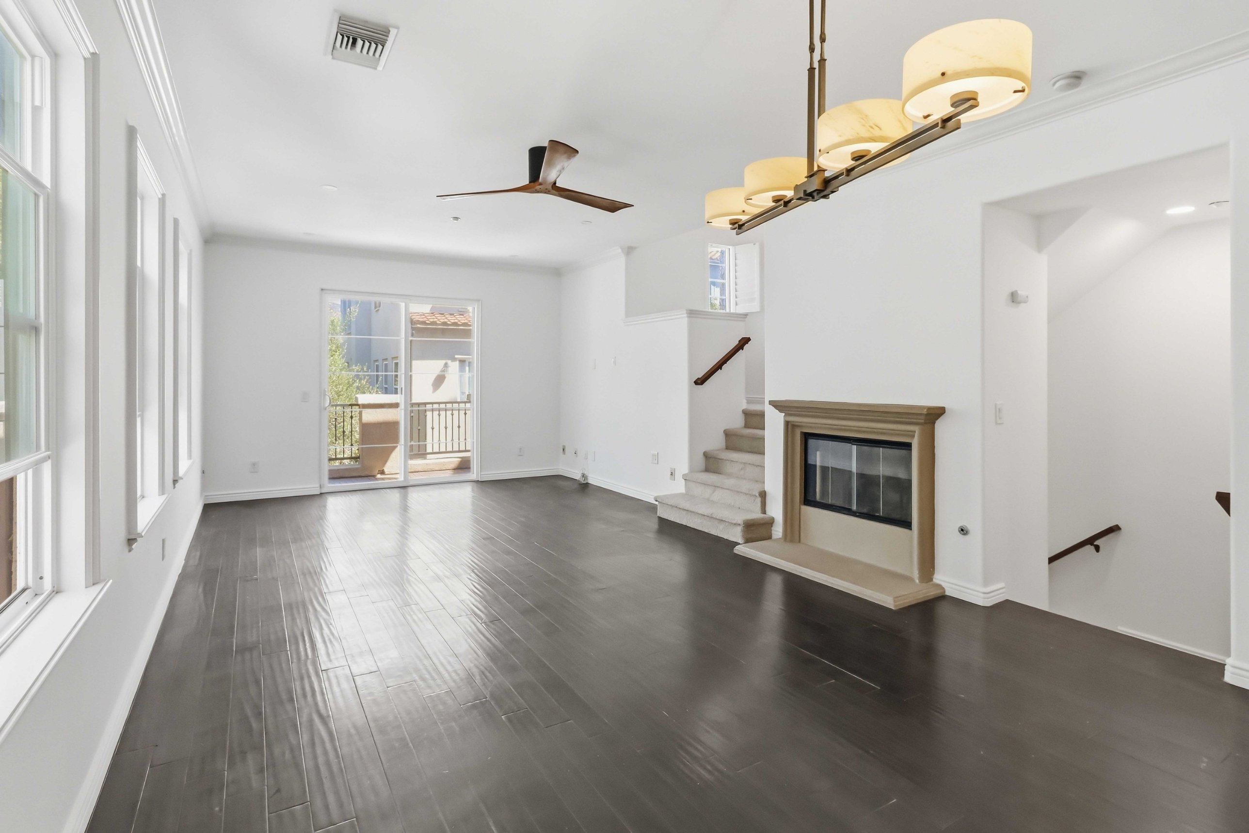 Main living level with chandelier, three large windows, dark hardwood floors.