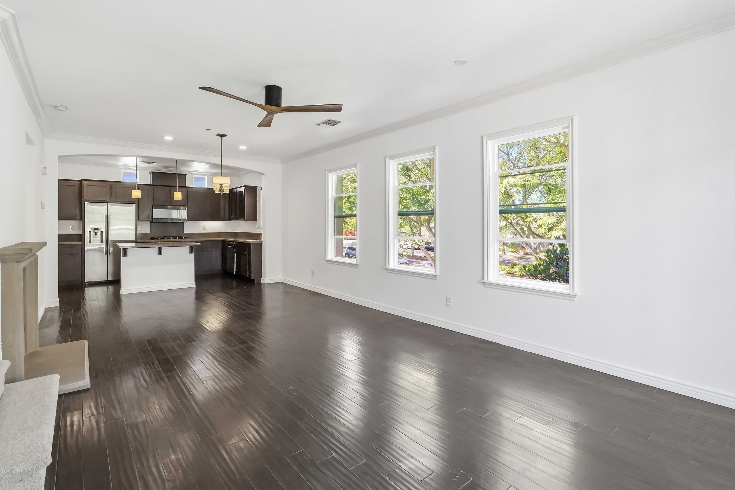 Main living level with dark hardwood floors, three large windows, and sightline through to the kitchen.