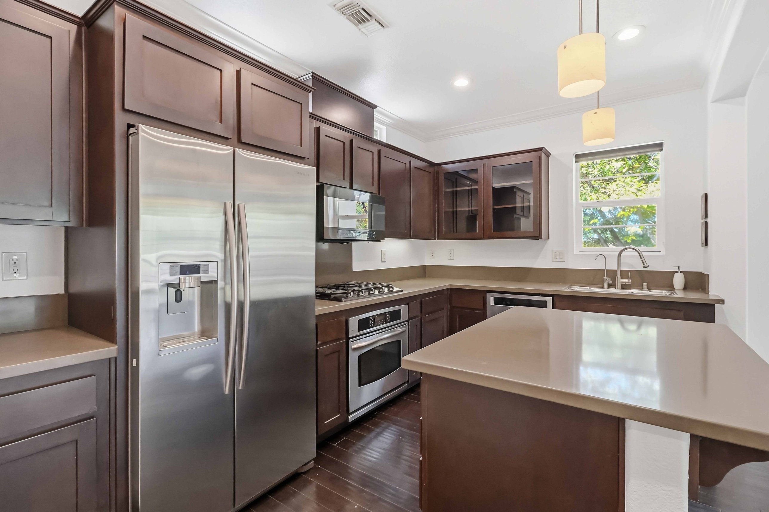Full kitchen with a center island, dark wood cabinets, stainless appliances, and pendant lighting.